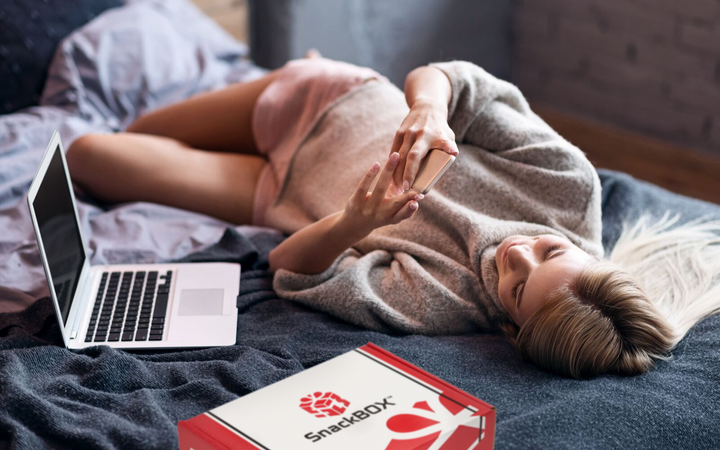 College student., laying on bed with snackbox