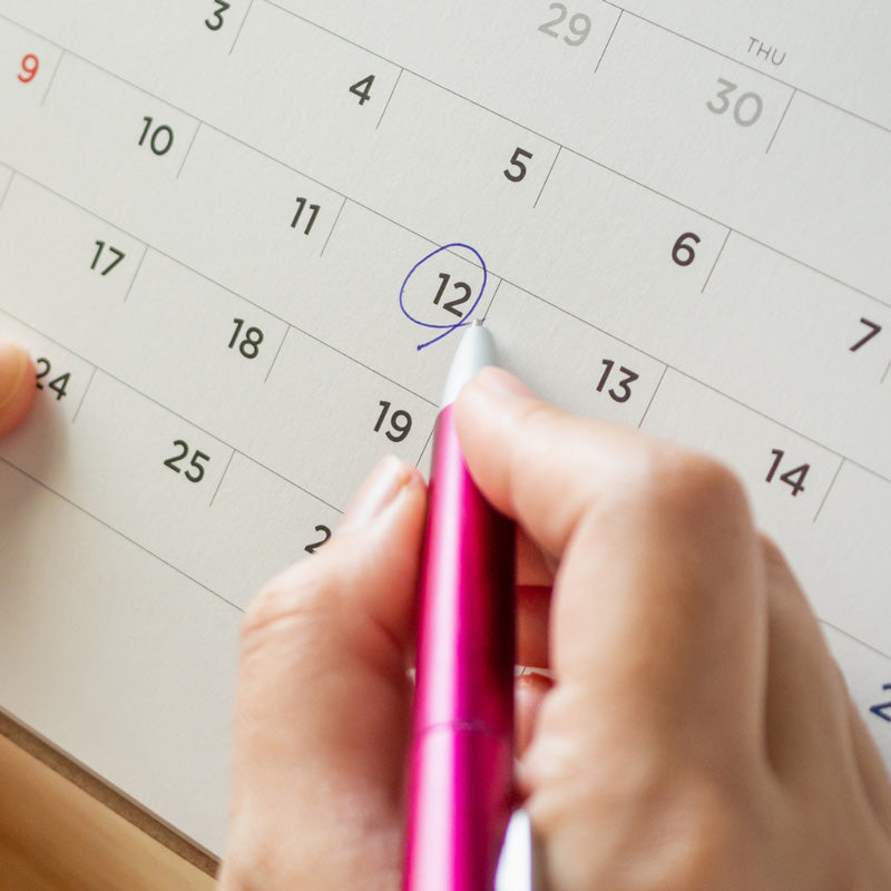 Person holding a pink pen and circling a date on the calendar