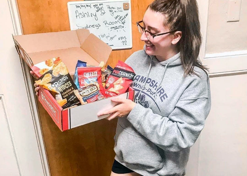 Female college student girl holding a SnackBOX in front of her dorm room door
