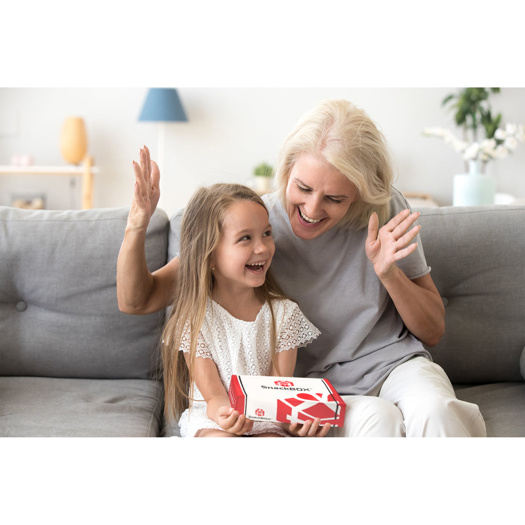 grandma and granddaughter on couch opening snack box with excited faces